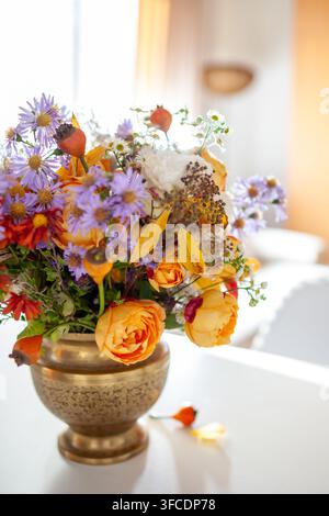 Close up of floral arrangement in brass vase. Fall interior decor of living room. Home decorated for autumn with bouquet of roses, aster flowers Stock Photo