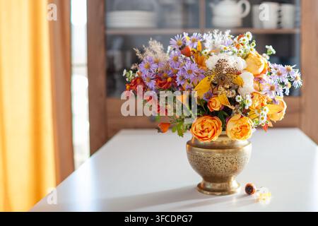 Close up of floral arrangement in brass vase. Fall interior decor of living room. Home decorated for autumn with bouquet of roses, aster flowers Stock Photo