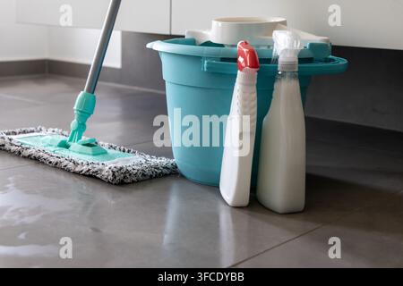 A modern mop with a turquoise handle and microfiber head is positioned next to a blue bucket and two white spray bottles filled with cleaning solution Stock Photo