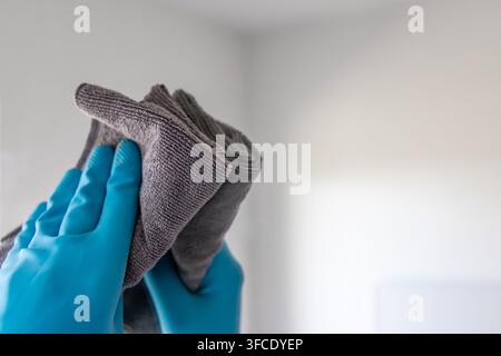 A close-up shot shows hands protected by blue rubber gloves meticulously cleaning a surface with a soft gray microfiber cloth Stock Photo
