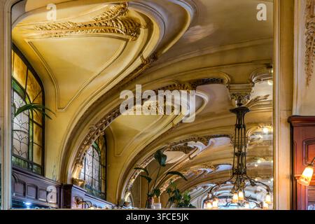 Richly ornamented, vaulted ceiling decoration with floral Art Nouveau motifs is reflected repeatedly in mirrored walls at the Brasserie Excelsior in Nancy, Grand Est, France; a wrought-iron chandelier and coloured glass windows are part of the original 1911 interior. Stock Photo