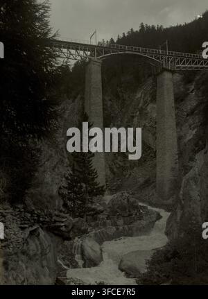 Film negative with recording of Zermatt, negative, photograph, Zermatt, 1921, photographer, plastic, organic material, cellulose nitrate film, gelatin silver negative, gelatin silver negative on cellulose nitrate film, height 90 mm x width 120 mm., A tall bridge spans a rocky gorge, supported by two massive stone pillars rising from the cliff faces, with metal trusses and railings along the deck; below, a turbulent stream flows over stepped rock ledges and around large boulders, creating cascades and white water; steep rock walls and a dense stand of evergreen trees flank the gorge, with a Stock Photo