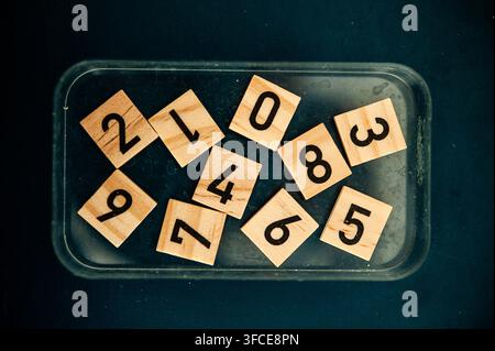 Wooden number tiles scattered in a clear tray on a dark surface, creating a playful mathematics and numeracy concept Stock Photo