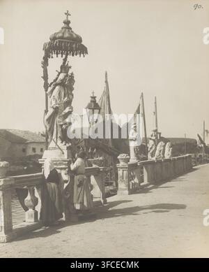 Two girls in front of a Madonna statue in Chioggia, Chioggia - Madonna Refugium Peccatorum, photograph, number: '90.', number: '3108.', photographer: Neue Photographische Gesellschaft, Chioggia, c. 1900, paper, pasteboard, gelatin silver print, developing gelatin silver print, height 243 mm x width 192 mm, Mary with the Christ-child., A stone balustrade runs along a waterfront with a group of carved statues and decorative urns lined on top, including a large crowned statue beneath a fringed canopy; several tall poles and nets rise behind the railing, and a vintage street lamp with a small Stock Photo