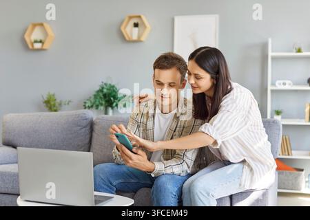 Young family couple using a laptop computer and an online banking on their smartphone Stock Photo