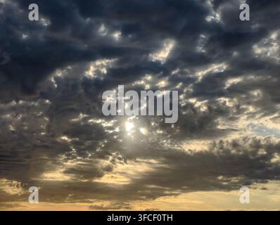 A dramatic, moody sky where golden sunlight pierces through thick, dark storm clouds, creating a powerful atmosphere of hope and resilience. Stock Photo