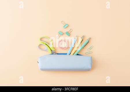Pastel stationery supplies arranged around a blue pencil case on a peach background, with ample copy space for school, office, study and creative conc Stock Photo