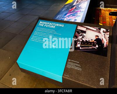 Manchester, UK - July 02, 2026: Museum exhibit panel titled Manufacturing the Future beside a technician operating industrial machine tools in Manches Stock Photo