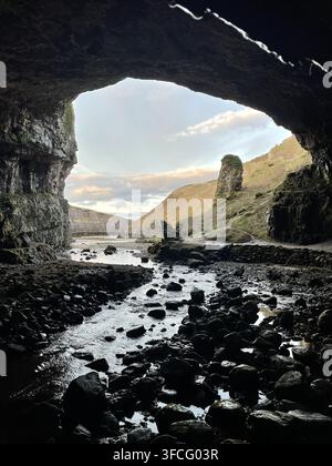 Dramatic view from inside Smoo Cave near Durness in the Scottish Highlands, looking across the rocky cave floor and stream toward the rugged landscape Stock Photo