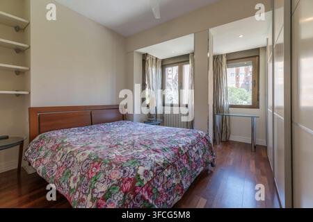 Same floral bedroom viewed from a different angle, showing built-in shelving, mirrored panels, and glass side tables with lamp. Stock Photo