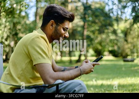 Young Indian Man Using Smartphone in Park Stock Photo