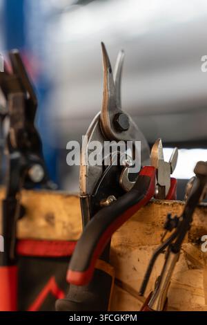 Repair tools rest in wooden holder with pliers and cutters pressed together in tight close up. Metal jaws, worn handles, and blurred workshop colors Stock Photo