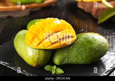 Sliced mangoes on a black slate plate with fresh whole fruit. Stock Photo