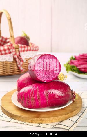 Red radishes on a plate with one cut open against a kitchen background. Stock Photo