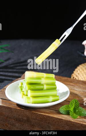 Fork holding a celery stick above a plate of cut celery on a dark background. Stock Photo