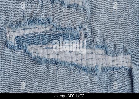 Detailed view ripped blue denim fabric with exposed white threads and distressed texture Stock Photo
