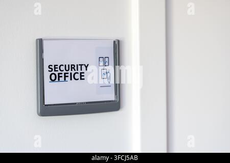 A clear sign on a white wall indicates the location of the security office with relevant icons Stock Photo