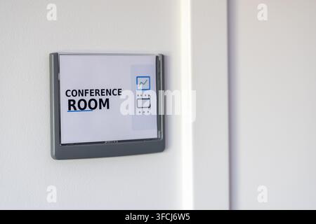 A minimalist sign indicating a conference room is mounted on a textured white wall next to a door frame Stock Photo