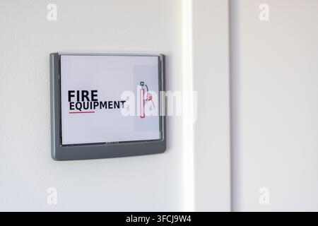 A clear sign with the words FIRE EQUIPMENT and an icon of a fire extinguisher is mounted on a white wall Stock Photo