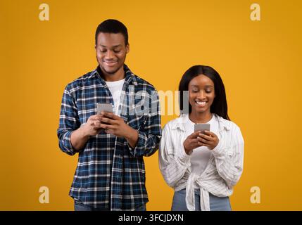 Modern virtual romantic relationships at social network. Happy young african american couple in love communicates using smartphones, isolated on yello Stock Photo