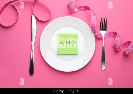 Paper note with word Anorexia, plate, cutlery and measuring tape on pink background, flat lay Stock Photo