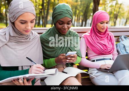 Modern Muslim Females Students Learning Using Phone And Laptop Outdoors Stock Photo