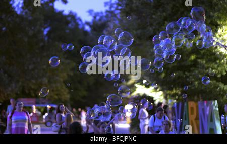 Iridescent soap bubbles drifting in the air at an outdoor event during a summer evening, with blurred people in the background. Bulgaria, varna, 27 au Stock Photo