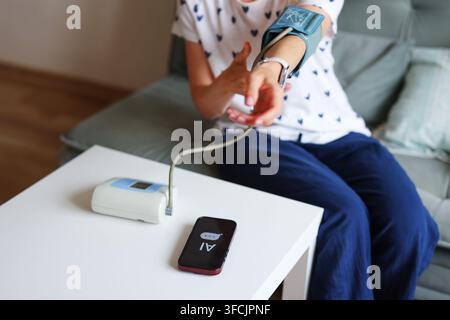 Patient uses AI chatbot for health advice while monitoring blood pressure at home instead of consulting a medical professional. Stock Photo