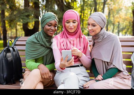 Muslim Students Ladies Using Smartphone With Educational App Sitting Outdoor Stock Photo