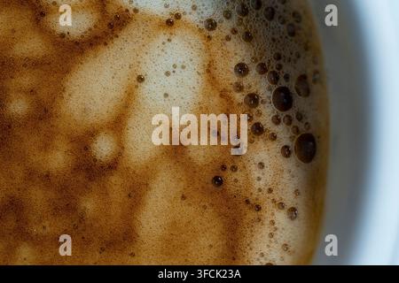Close up top view of hot espresso foam background. Rich brown coffee crema texture with small bubbles and swirls in white cup. Perfect morning energy Stock Photo