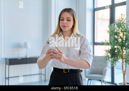 Focused business woman using smartphone standing in modern light office Stock Photo