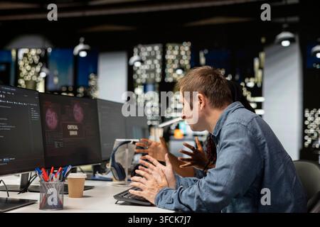 Software developer at office desk thinking how to fix critical error warning displayed on computer. Tech startup IT worker brainstorming how to fix co Stock Photo