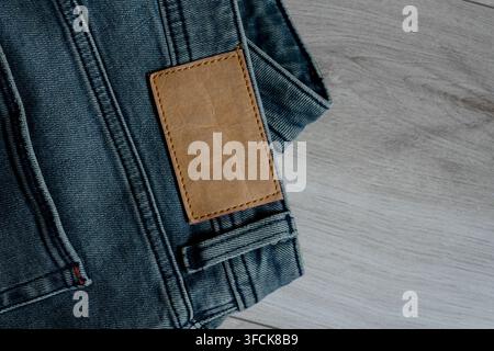 Blue denim fabric with a blank brown leather clothing label on a rustic wooden floor Stock Photo