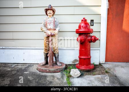 Vintage Firefighter Statue beside Fire Hydrant Sullivans Island | SULLIVAN'S ISLAND, South Carolina �� A painted cast-iron firefighter figure stands sentinel beside a fire hydrant at a former fire station on the island, now repurposed after the department relocated to its rebuilt Middle Street headquarters. The Sullivan's Island Volunteer Fire Department traces to 1948, funded ever since largely by an annual fish fry the volunteers still run each June. Stock Photo