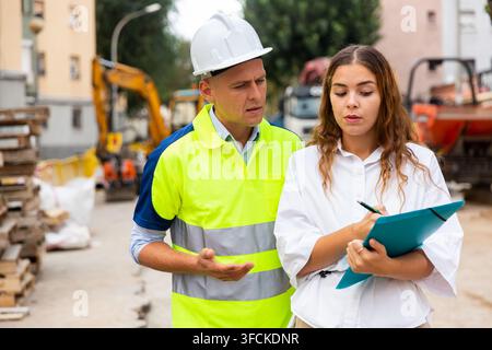 Man engineer and a young woman discuss a construction project while , taking important notes Stock Photo
