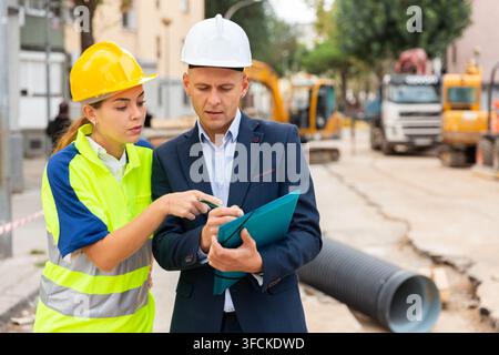 Civil engineer and a young woman worker discuss a construction plan Stock Photo