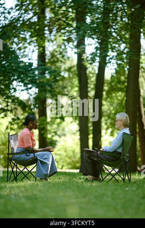 Vertical of Black Woman Having Therapy Session with Senior Therapist in Park Stock Photo
