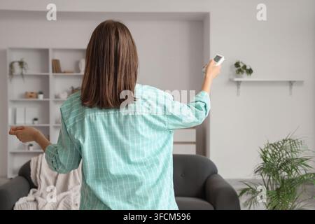 Climate control and energy efficiency, woman using air conditioner remote to adjust home temperature for comfort and sustainable living in modern room Stock Photo