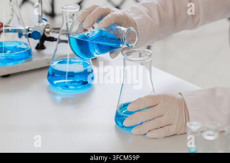 Scientific research and chemical experiment, scientist pouring blue liquid into glass flask for pharmaceutical development and laboratory analysis Stock Photo