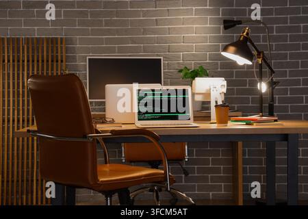 Software development and remote work, programmer workspace with laptop showing code at night in home office with desk lamp and coffee cup Stock Photo