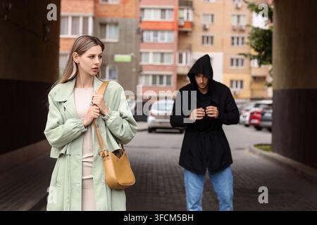 Personal safety and street crime, woman feeling anxious while being followed by a suspicious man in a hooded sweatshirt on a city street Stock Photo