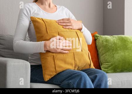 Comfort and relaxation at home, woman holding a soft yellow cushion on a sofa for stress relief and mental wellness in a cozy living room interior Stock Photo