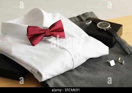 Formal wear and wedding attire, red bow tie with white dress shirt and grey trousers for groom or gala event preparation on a wooden table Stock Photo