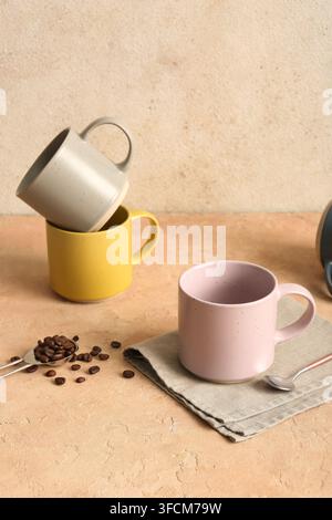 Ceramic mugs, napkin and teaspoon with coffee beans on pink table near light wall Stock Photo
