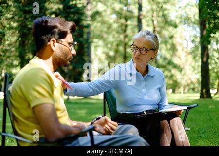 Senior Female Therapist Supporting South Asian Man in Outdoor Session Stock Photo