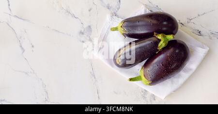 Healthy eating and fresh produce, three organic eggplants with water drops on a white napkin and marble background Stock Photo