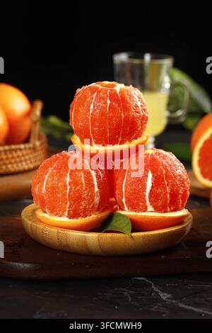 Peeled mandarins stacked on orange slices with dark blurred background. Stock Photo