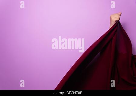 woman hand holding red silk fabric against purple background Stock Photo