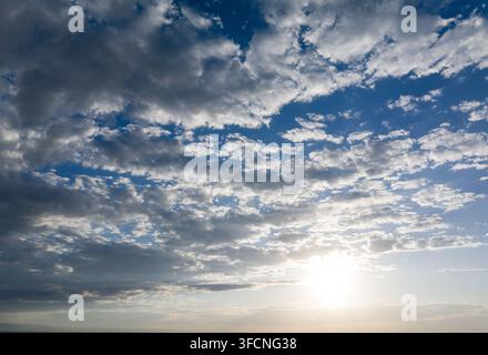 Sunlight pierces through scattered clouds on vast blue sky Stock Photo