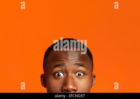 Closeup of african guy surprised eyes, orange background Stock Photo